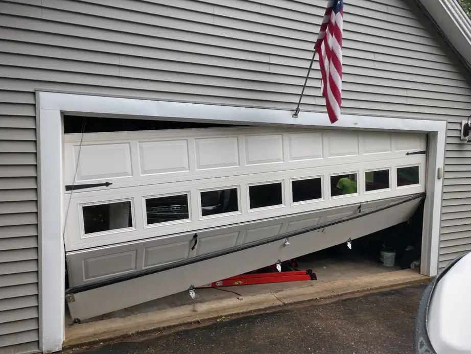 White garage door pushed off its track, the lower sections buckled inward