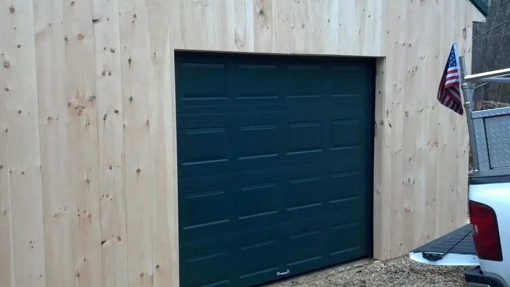 Dark green raised-panel garage door set into new pine siding