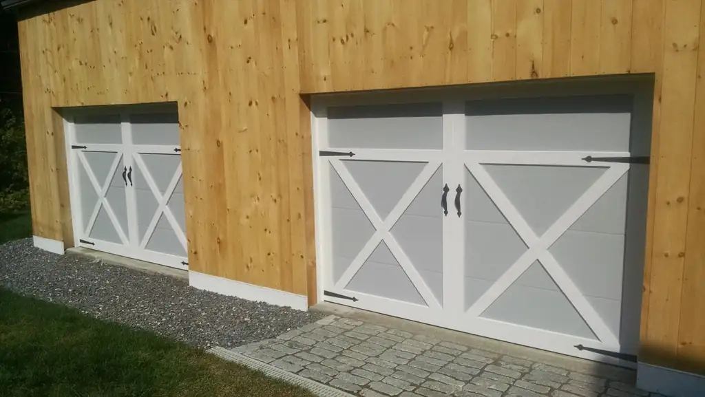 Two white X-brace carriage-style garage doors in a new pine-sided garage
